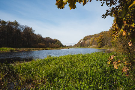 A picturesque view of a tranquil river flowing through vibrant greenery and autumn-colored trees, reflecting natures beauty in this peaceful setting that invites relaxation and explorationの写真素材