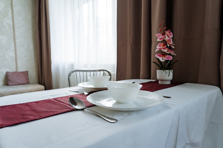 A beautifully arranged dining table with a crisp white tablecloth, exquisite dishware, and floral decor creates a warm atmosphere, ideal for an enjoyable dining experience that unites peopleの写真素材