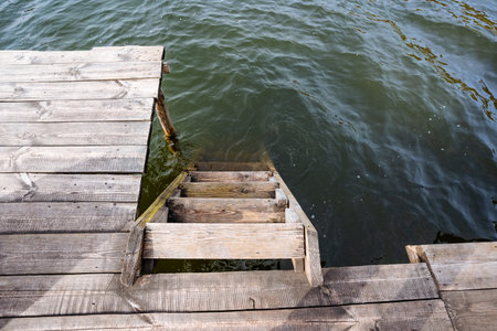 A wooden dock is equipped with sturdy stairs that lead down into the shimmering water below, creating a spot for relaxation and scenic views of natureの写真素材