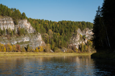 Imagine a picturesque lake that is beautifully surrounded by majestic mountains and lush green trees, all under a bright and sunny sky, creating a perfect scene of natures beautyの写真素材