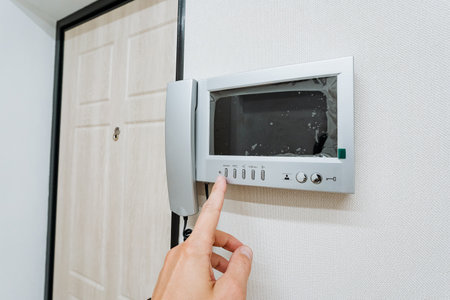 This image showcases a modern intercom system mounted on a wall, with a finger poised to press a...