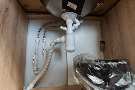 Examine a modern undersink plumbing installation featuring organized pipes, efficient drainage systems, and quality materials for a clean, functional kitchen, perfect for contemporary livingの写真素材