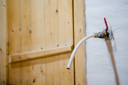 A detailed view of a pipe connected to a wall-mounted water valve, featuring a striking red handle, set against a rustic wooden door background, perfect for plumbing or home renovation imagery.の写真素材