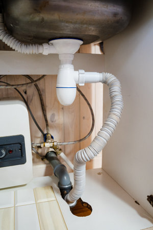 This image showcases a detailed view of an under-sink plumbing system, including essential components like the waste pipe and connection to the water heater, highlighting home maintenance.の写真素材