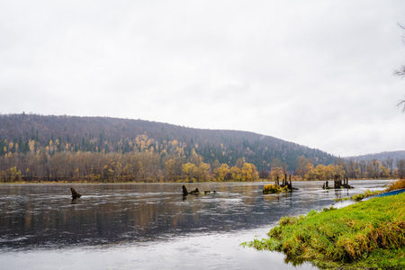 In a serene river scene, autumns vibrant colors reflect in calm waters. Misty mountains rise in the distance, enhancing the beauty of this tranquil landscape, inviting nature lovers to exploreの写真素材