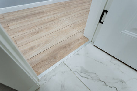 modern bathroom floor transition showing marble tile meeting oak laminate clean threshold detail...