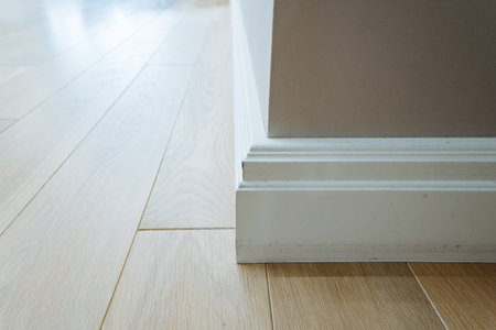 A detailed view of light wooden flooring seamlessly meeting a pristine white baseboard, beautifully showcasing a clean and contemporary aesthetic in a welllit and inviting indoor spaceの写真素材
