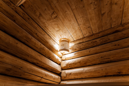 warm wall lamp highlighting log joinery and wood grain, cozy golden glow accentuating rustic craftsmanship and clean well maintained spa interiorの写真素材