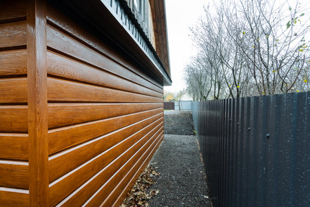 narrow service path beside glossy woodclad wall and metal fence, maintenance crew access for...