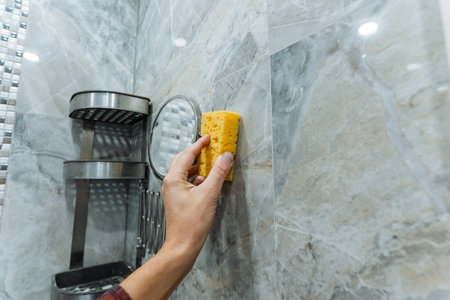 mirror cleaning scene, using yellow sponge to wipe mirror, soft light highlights fingerprints and grout dust removal, mirror being cleaned with sponge against marble and mosaic backgroundの写真素材