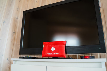 In a stylish contemporary living room, a bright red first aid kit is placed on a TV stand, emphasizing the importance of safety and preparedness in homes for everyoneの写真素材