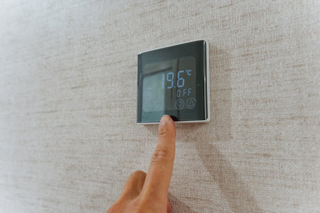 thermostat adjustment scene, digital thermostat control in modern apartment, fingertip pressing...