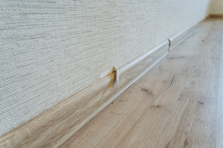 detached baseboard leaving gap above laminate flooring near corner visible adhesive failure slight wall damage and dust accumulation highlighting finishing issue and need for skirting repairの写真素材