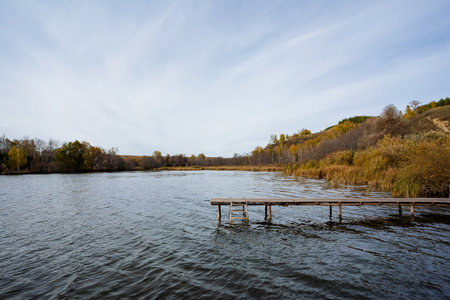 In the midst of a serene lake, there is a sturdy wooden dock that extends out over the water, inviting those who wander nearby to admire the natural beauty surrounding this peaceful areaの写真素材