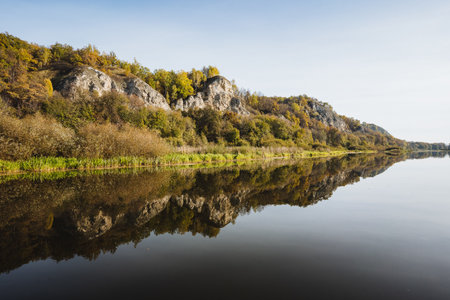 A tranquil river scene showcases the reflection of rocky cliffs and vibrant autumn foliage, highlighting natures beauty and serene essence, perfect for exploration and outdoor adventureの写真素材
