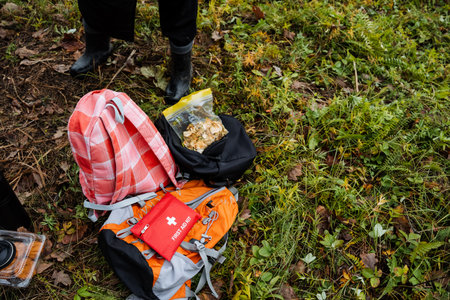 backpack gear on mossy ground with visible medical pouch, hiking boots standing nearby, map and supplies spread for quick assessment, overcast light, autumn leaves, searchand-rescue practiceの写真素材