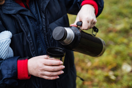 leader offers hot beverage outdoors, individual gives hot beverage to kids during outdoor activityの写真素材