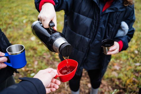 hot drink pouring, person pouring hot drink into red cup during outdoor relaxing break in grassyの写真素材