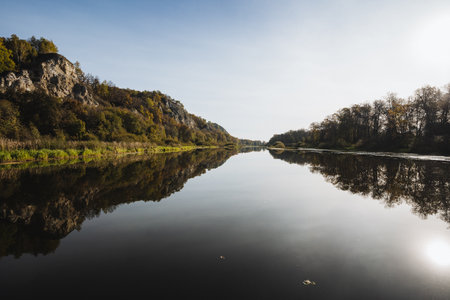 This picturesque view showcases a serene river reflecting majestic cliffs and lush trees under a stunning dawn sky, ideal for nature and landscape photography enthusiasts capturing outdoor beautyの写真素材