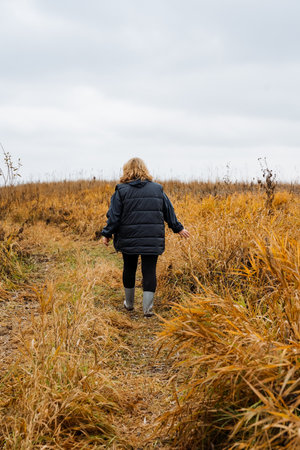 woman carefully navigating tall marsh grasses, woman walks steadily through dense marshland grassesの写真素材