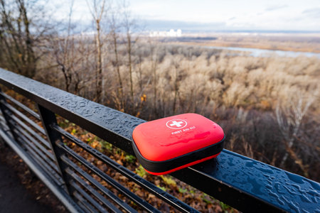 Red first aid kit on railing overlooking marsh at sunrise, dewspeckled metal, distant river bend,...
