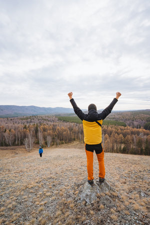 Inspiring team gathering, Overlook scene with enthusiastic team leader, Individual raising arms to encourage rally below, Person in yellow jacket motivates team amidst natural rocky terrainの写真素材