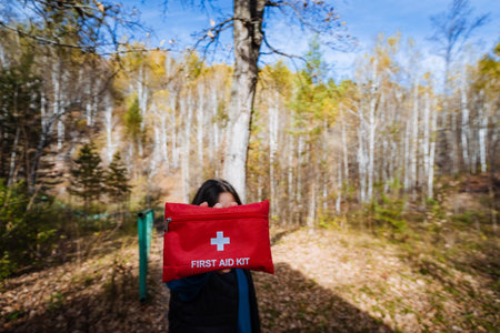 In a vibrant, lush forest, a person can be seen holding a bright red first aid kit, which emphasizes the crucial importance of being prepared and maintaining safety during various outdoor activitiesの写真素材