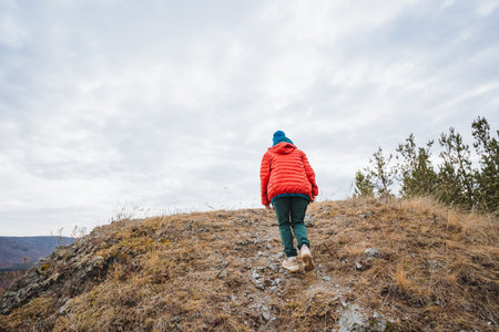 Child hiking confidently, Young girl ascends rugged hillside, Boy carefully navigates rocky mountain path, Young explorer methodically ascends rough terrain with autumn leaves under warmの写真素材