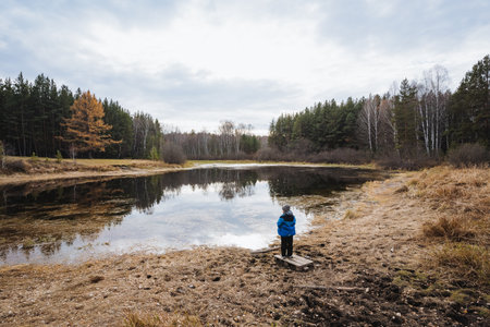 Individual in blue gazing over pond, Solitary person reflects beside tranquil pond amid trees, Lone...