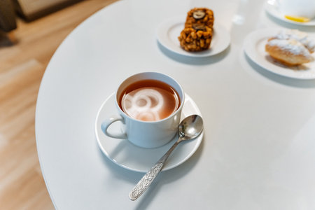 cappuccino with heart latte art on white table, saucer and spoon beside small plates of pastries, soft natural light, clean minimal cafe aesthetic, warm creamy foam, inviting breakfast moodの写真素材