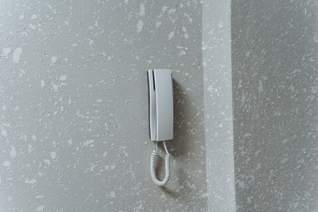 white corded handset on speckled wall evoking retro communication aesthetic, mounted intercom style with soft shadows and muted gray tones, textured plaster backdrop, suited for interior design,の写真素材