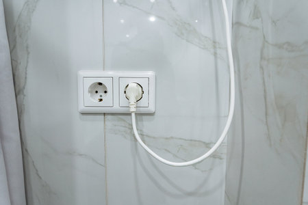 shiny tiled bathroom safety details, closeup of marble surfaces highlighting electrical safety features, detailed view of polished marble walls showing electrical socket and safety reflectionsの写真素材