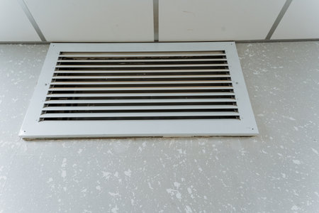 white ceiling vent grille overhead in tiled office, subtle dust on metal slats, fluorescent lighting...