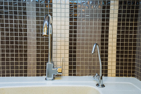 dual faucet with filtered water spout and chrome finish against mosaic tile, close-up showing soap dispenser and precise spout curvature, modern eco and hygiene focused kitchen fixture idealの写真素材