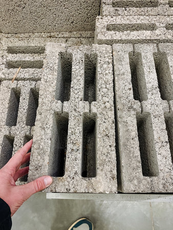 hand holding cinder block in aisle for masonry selection, close-up of hollow core and rough concrete...