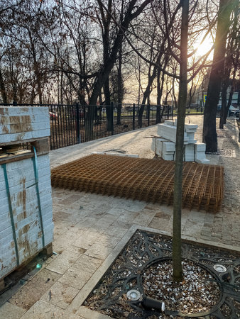 pallets of construction mesh on patio staged for garden renovation at sunset, large roll of mesh beside stacked block pallets, paved courtyard with young trees, warm backlight and long shadows,の写真素材