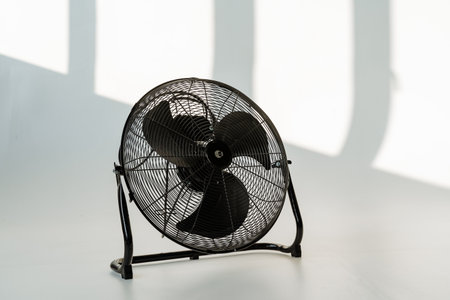 black metal fan on floor, retro industrial tabletop design casting angular shadows across white...