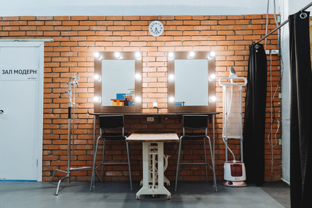 brick wall vanity mirrors with lights and stools. industrial studio styling area featuring twin lighted mirrors, metal stools, equipment racks, curtain backdrop, clock on brick, cables and steamer,の写真素材