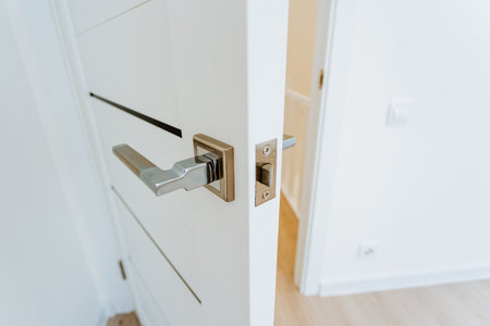 white door slightly open showing latch and chrome handle, closeup of lock mechanism and hinge, clean...