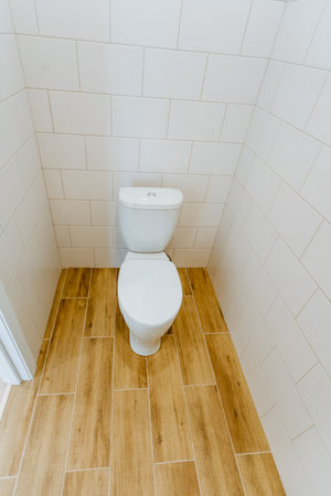 small tiled bathroom with toilet and wooden floor, clean minimalist corner layout, white porcelain bowl and cistern, bright grout lines, practical compact design ideal for rental or small apartmentの写真素材