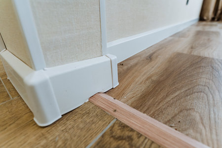 detailed shot wooden spacer creating expansion gap at baseboard during installation; installer...