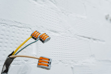 closeup of wire connectors in wall cavity, orange push-in terminals attached to yellow and gray cables, crisp white brick texture and wooden floor, product-style composition suited for catalogue,の写真素材
