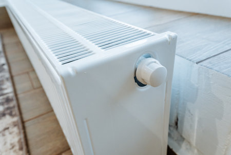 heating valve control, white panel radiator featuring adjustable temperature knob, focus on temperature regulation through adjustable radiators adjacent to laminate flooring and baseboardsの写真素材