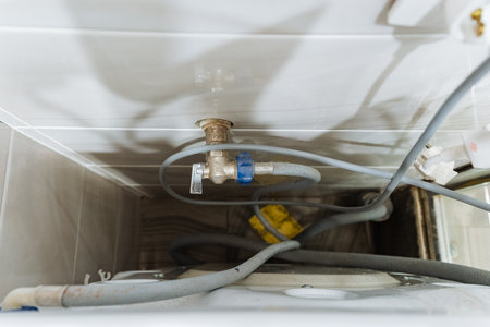 exposed plumbing access behind cabinet, valves and flexible hoses visible, compact service cavity, connector and drain layout, maintenance ready, renovation detail in bathroom utility space.の写真素材