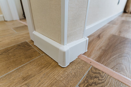 close-up white corner guard installed on wall base for safety and childproofing; installer securing...