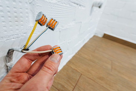 hand connecting wires with orange push-in connectors on white brick background, close focus on...