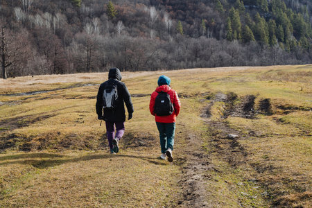 Two hikers walking through meadow, backpacks and beanies, conversation and easy pace under overcast...