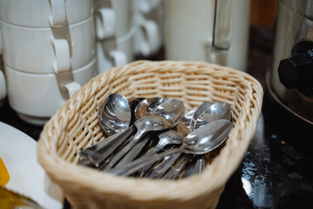 Silver Spoons In Wicker Basket Arranged On Black Countertop Near Buffet Station, Polished Stainless...