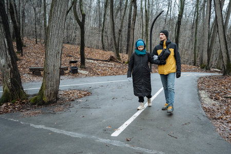father walking with child on wet trail, matching jackets and friendly gestures, gray sky,...