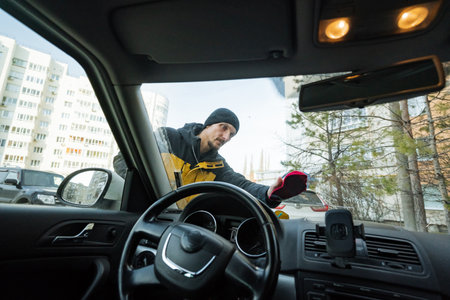 cleaning windshield before journey, man wiping car windshield in city background, person preparing...